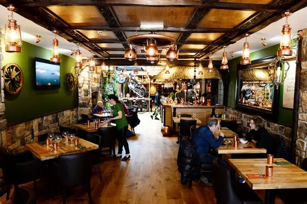 The dining room at Herb Restaurant with wooden tables, lanterns and green walls